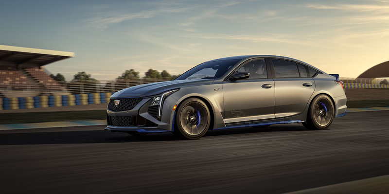 A sleek, silver sports sedan speeds along a racetrack at sunset. The car's modern design and motion convey power and excitement against a blurred background.